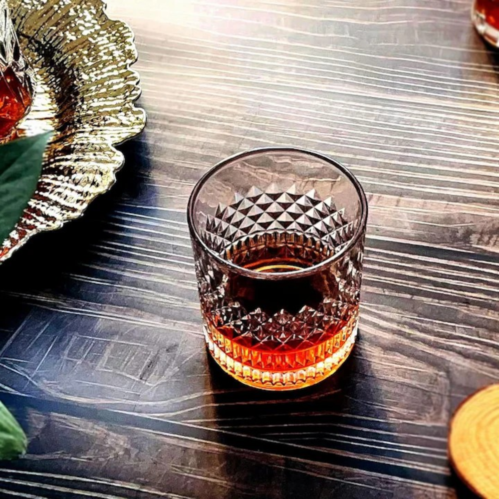 Pahar din cristal masiv MADGENIX Noble umplut cu whisky fin si o sfera mare de gheata stralucitoare, asezat pe o suprafata