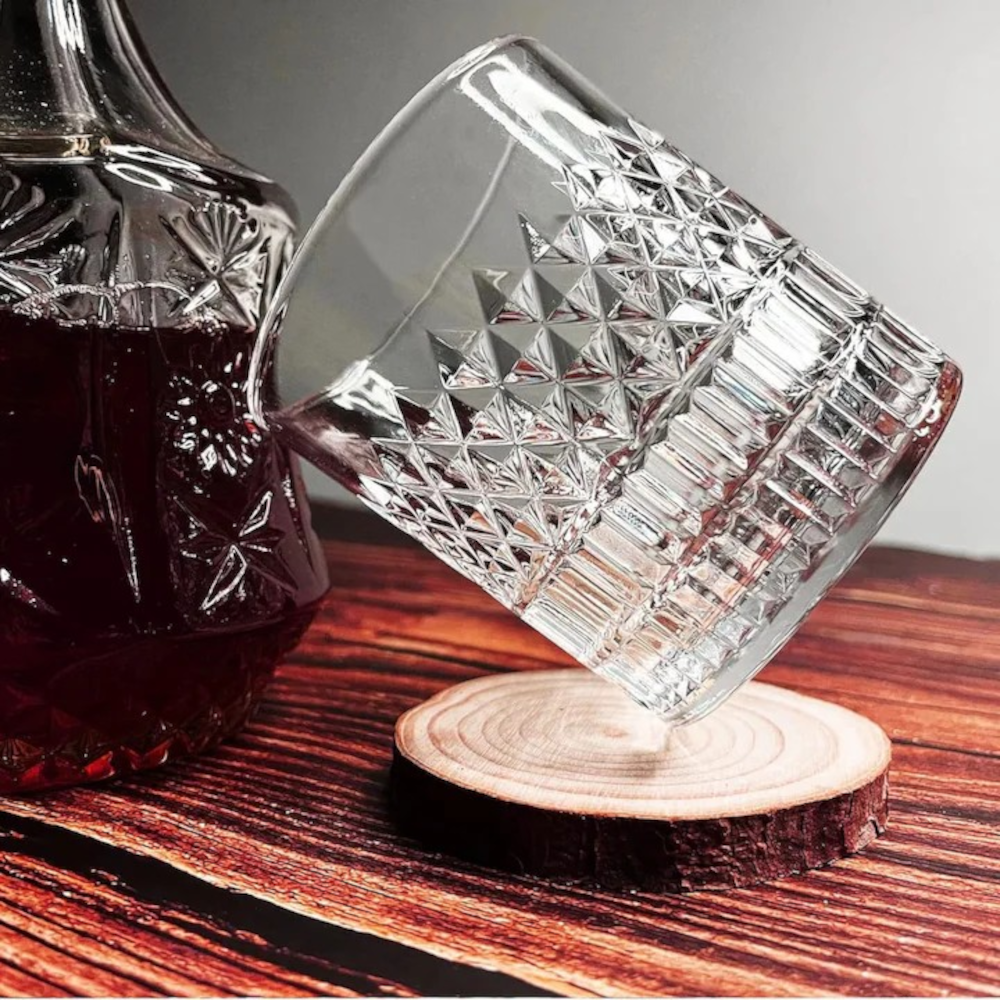 Pahar din cristal masiv MADGENIX Noble umplut cu whisky fin si o sfera mare de gheata stralucitoare, asezat pe o suprafata lucioasa de bar.