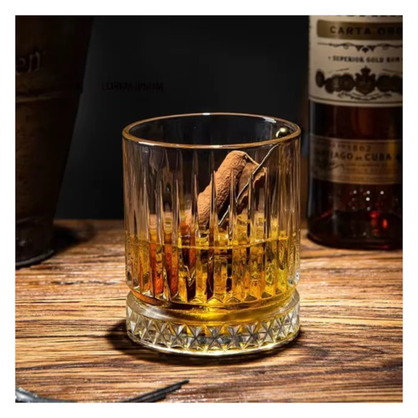 Detaliu al unui pahar de whiskey din sticla transparenta cu dungi in relief, continand bautura si gheata, asezat pe o felie decorativa de portocala.