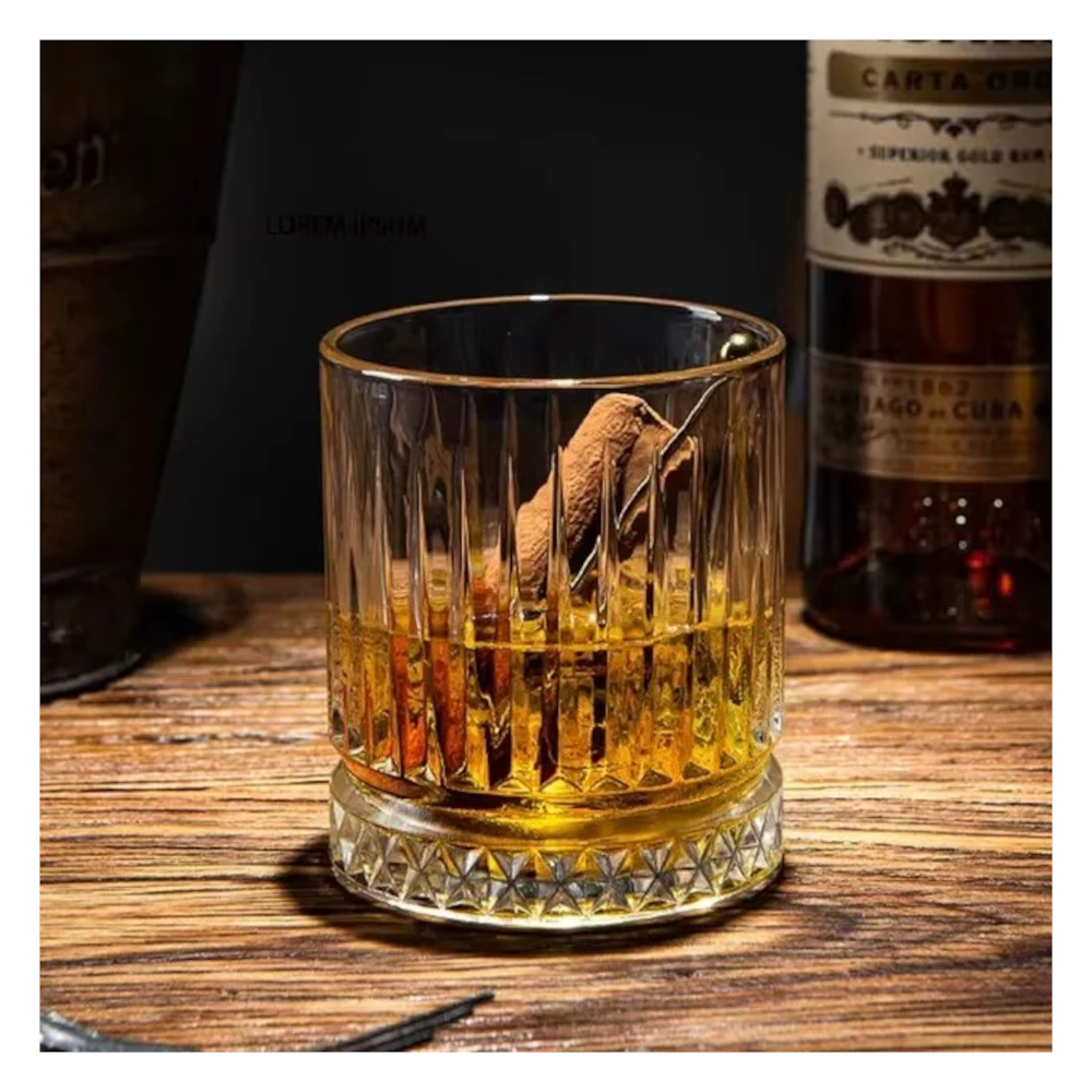Detaliu al unui pahar de whiskey din sticla transparenta cu dungi in relief, continand bautura si gheata, asezat pe o felie decorativa de portocala.