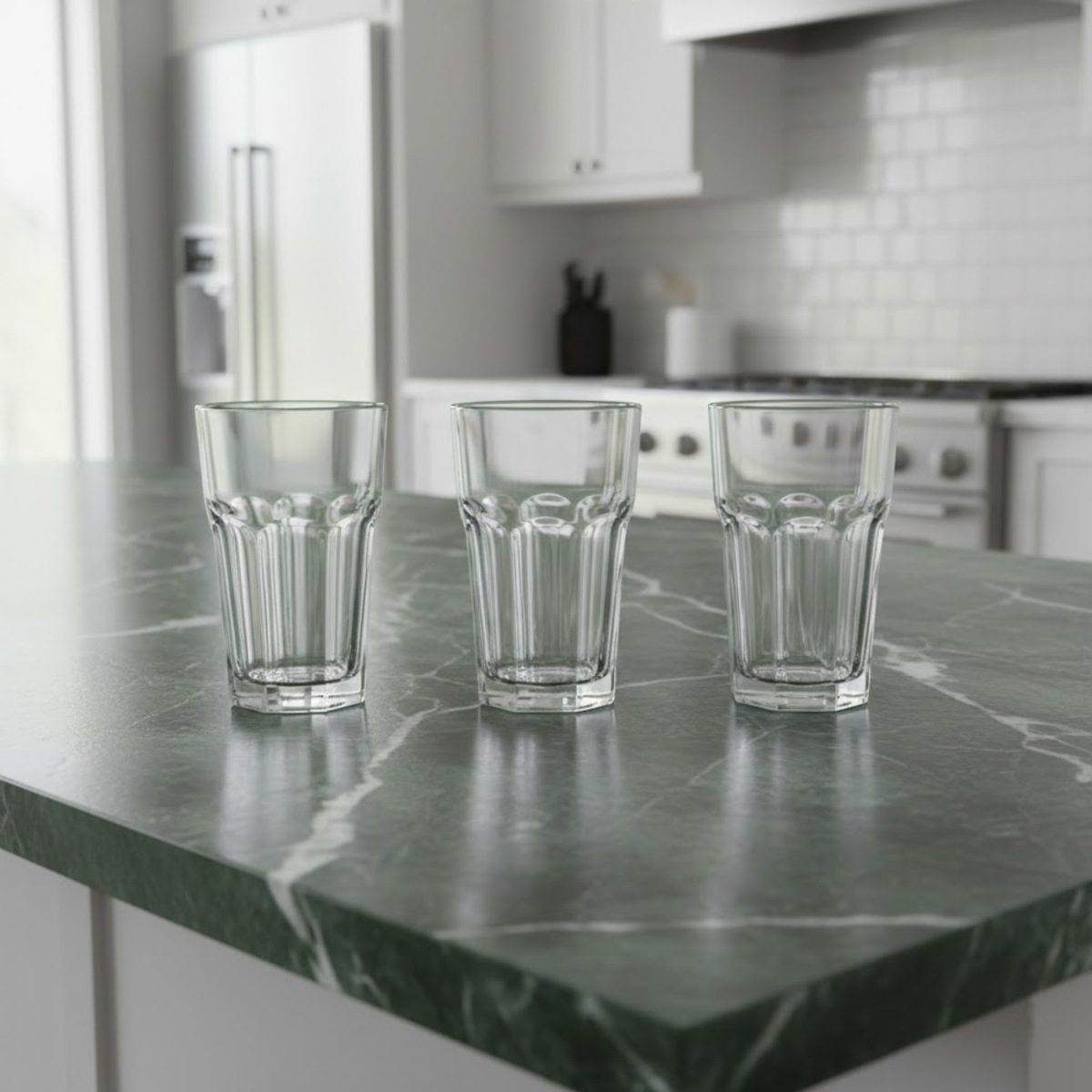 Trei pahare Highball din sticla transparenta cu model fatetat la baza, asezate pe un blat modern de bucatarie din marmura verde.