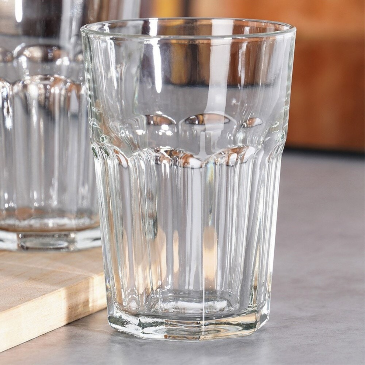 Pahar inalt din sticla transparenta cu model fatetat prezentat de aproape pe o masa de bar, evidentiind baza masiva stabila.